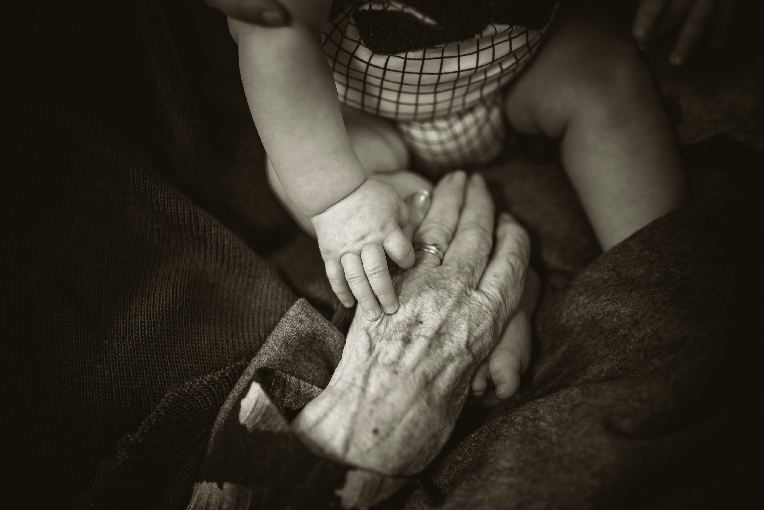 Generational connection symbolized by a baby holding an elderly hand, representing family, legacy, and inheritance planning.